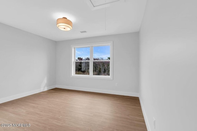 unfurnished room featuring light wood-style flooring, attic access, baseboards, and visible vents