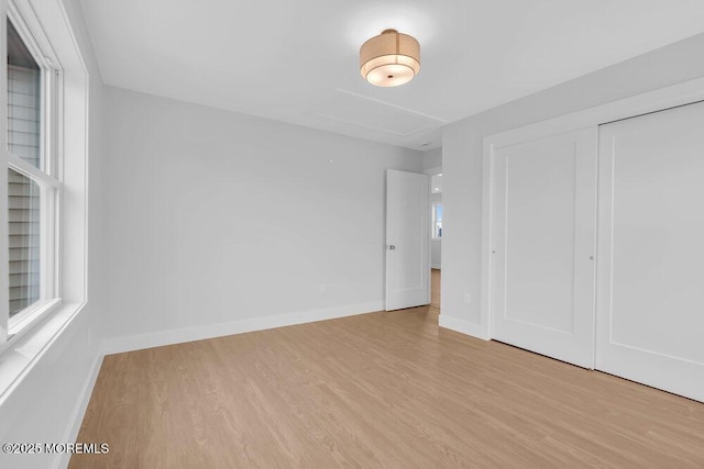 unfurnished bedroom featuring light wood-type flooring, a closet, attic access, and baseboards