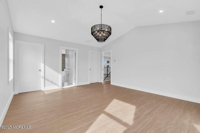 spare room featuring a chandelier, vaulted ceiling, and light wood-style flooring
