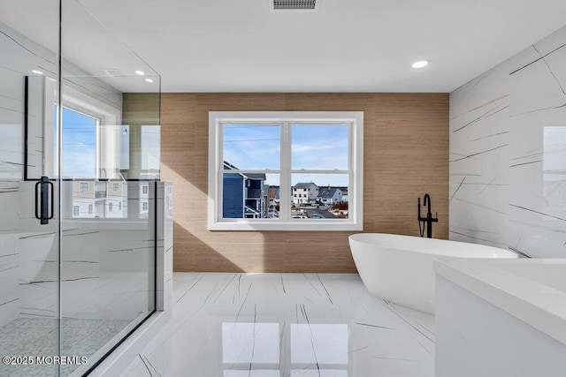bathroom with tile walls, a freestanding bath, marble finish floor, and a stall shower