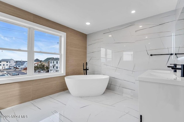 full bath with a soaking tub, vanity, recessed lighting, marble finish floor, and tile walls