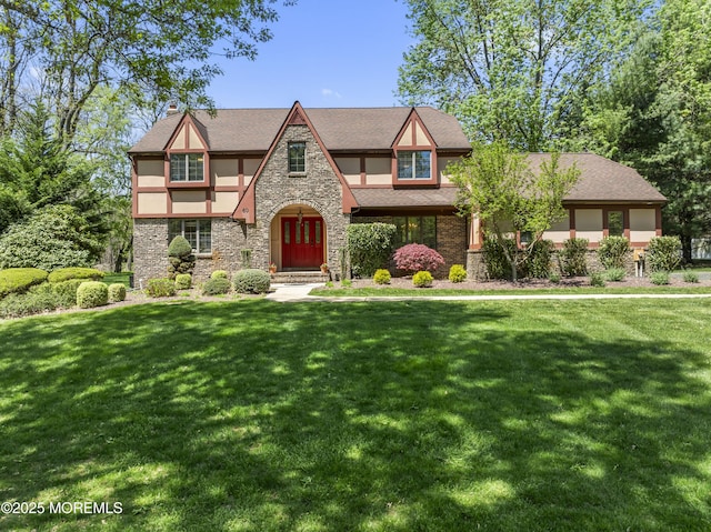 tudor home with a chimney, stucco siding, a front yard, and stone siding