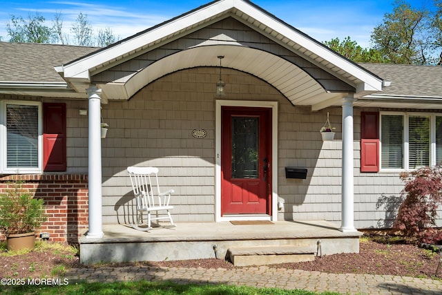 doorway to property with a porch and roof with shingles