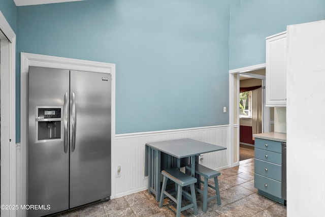 kitchen with light countertops, baseboards, stainless steel fridge, and a wainscoted wall