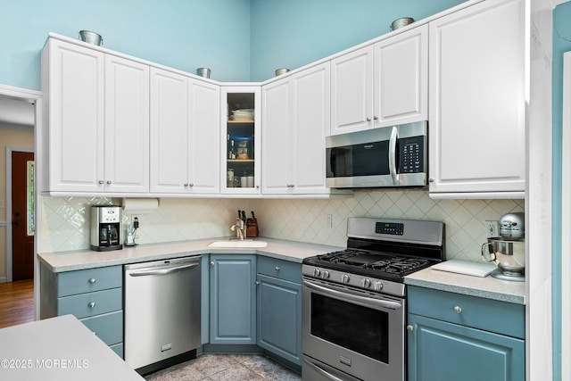kitchen with decorative backsplash, light countertops, white cabinets, glass insert cabinets, and stainless steel appliances