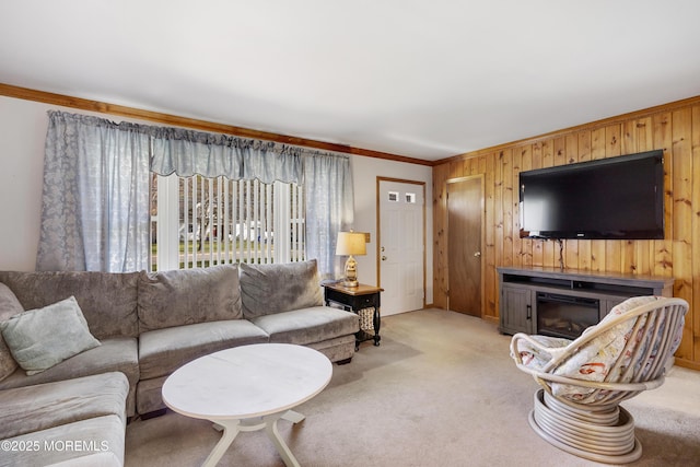 carpeted living room featuring crown molding, wood walls, and a glass covered fireplace