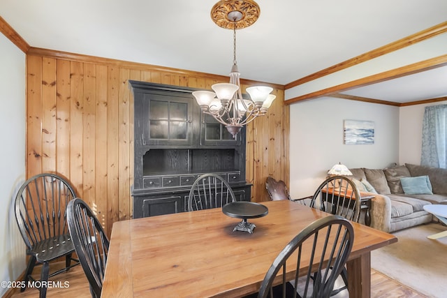 dining space with ornamental molding, wooden walls, a notable chandelier, and light wood finished floors