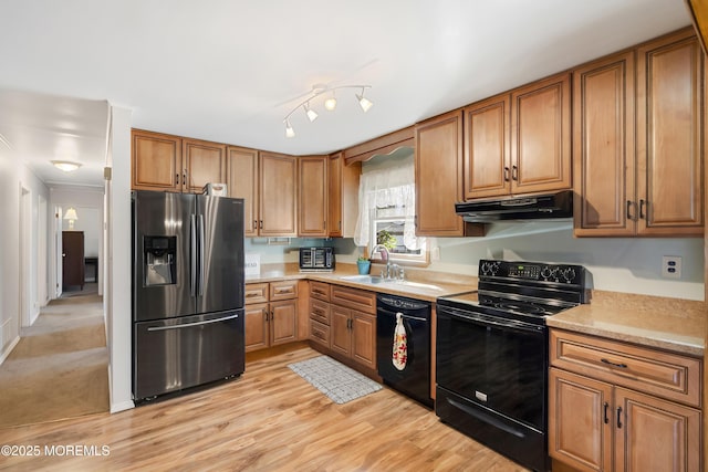 kitchen featuring light countertops, under cabinet range hood, a sink, black appliances, and brown cabinetry