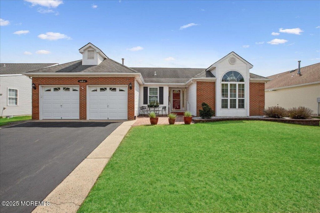 ranch-style home featuring aphalt driveway, an attached garage, brick siding, a front lawn, and roof with shingles