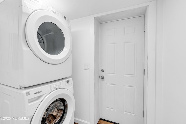 laundry room featuring baseboards, wood finished floors, stacked washer and clothes dryer, and laundry area