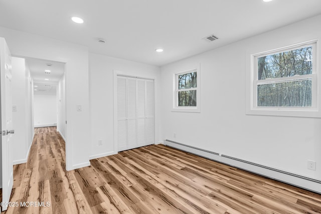unfurnished bedroom featuring a baseboard heating unit, a closet, light wood finished floors, and recessed lighting