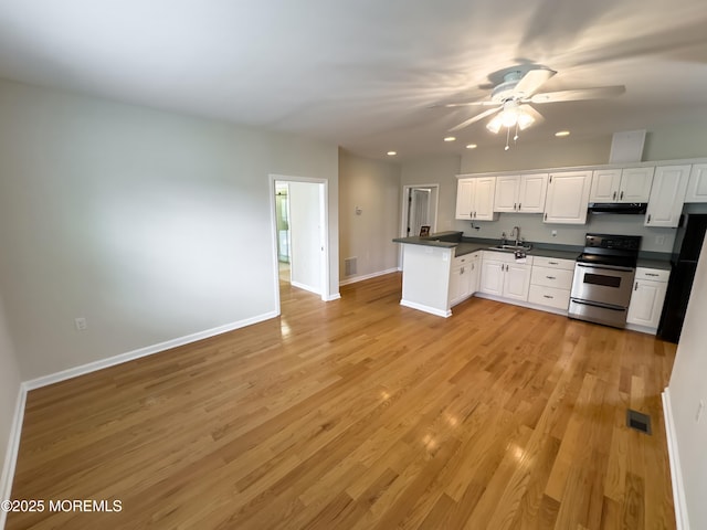 kitchen featuring dark countertops, a sink, stainless steel range with electric cooktop, a peninsula, and freestanding refrigerator