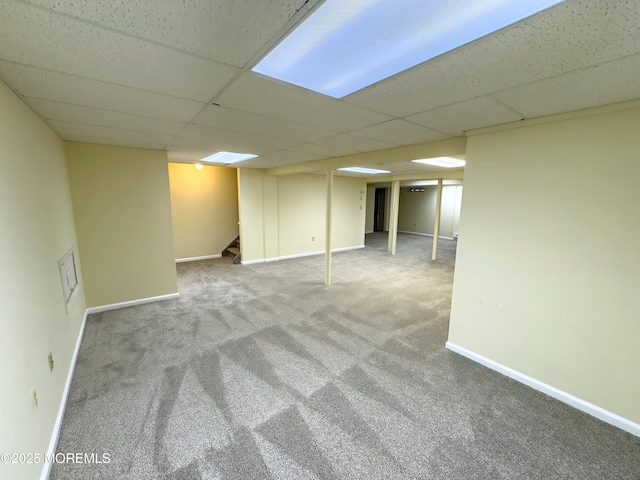 finished below grade area featuring carpet, a drop ceiling, baseboards, and stairway
