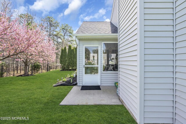 view of exterior entry with a patio area, roof with shingles, and a yard