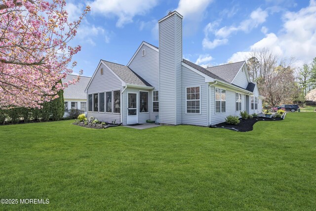 rear view of house with a chimney, a sunroom, a yard, and a shingled roof