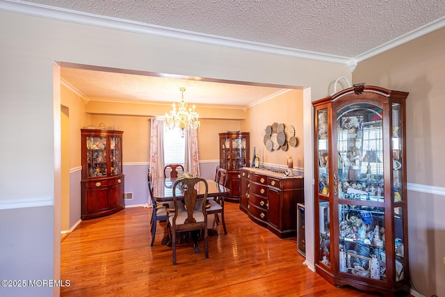 dining space with crown molding, an inviting chandelier, hardwood / wood-style flooring, and a textured ceiling