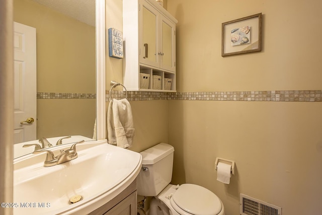 bathroom featuring toilet, a sink, and visible vents