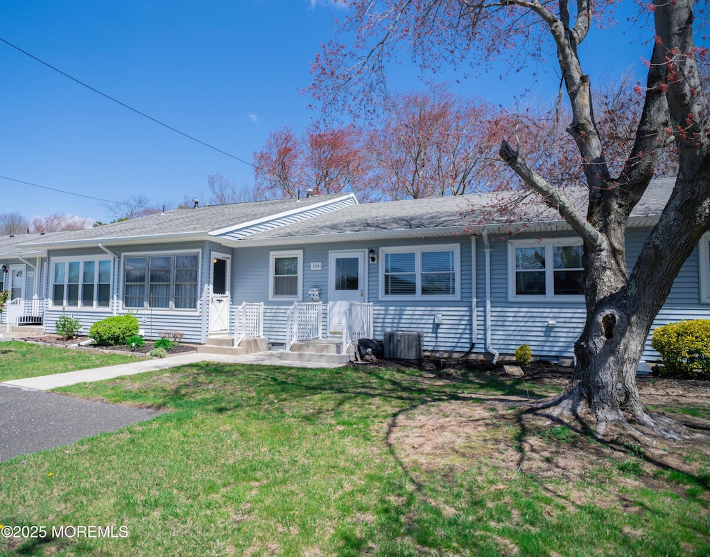 view of front of home featuring cooling unit, roof with shingles, and a front yard