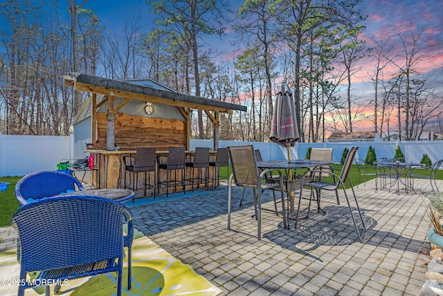 patio terrace at dusk featuring a water view, fence, outdoor dry bar, and outdoor dining area