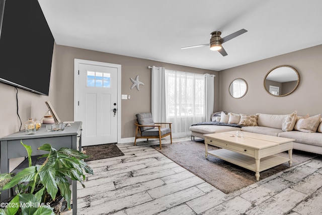living room featuring baseboards, light wood-type flooring, and a ceiling fan