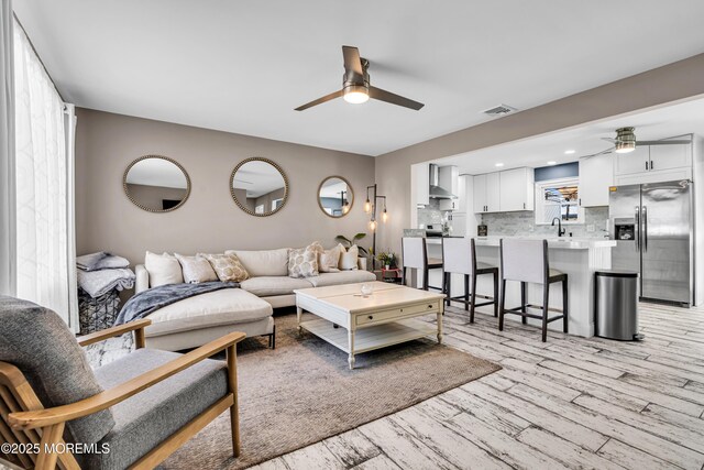 living room featuring visible vents, a ceiling fan, and light wood finished floors