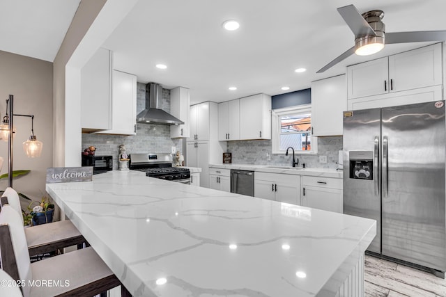 kitchen featuring wall chimney range hood, a sink, light stone counters, and appliances with stainless steel finishes