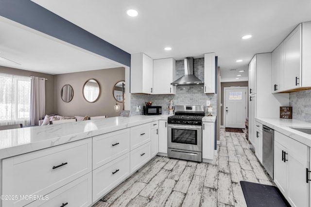 kitchen featuring plenty of natural light, wall chimney exhaust hood, light stone counters, and stainless steel appliances