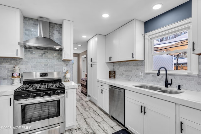 kitchen with tasteful backsplash, wall chimney range hood, white cabinetry, stainless steel appliances, and a sink