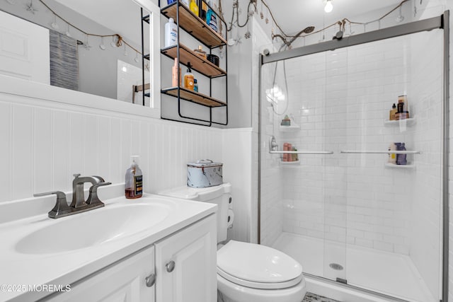 bathroom with toilet, a shower stall, wainscoting, and vanity