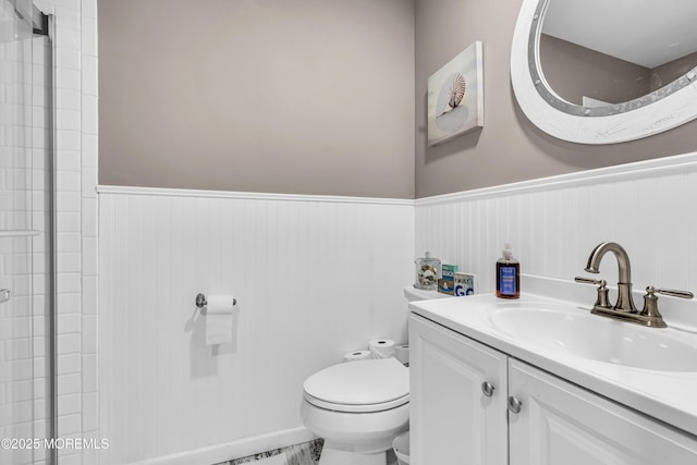 bathroom with toilet, vanity, and a wainscoted wall