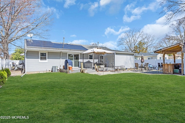 rear view of property with a patio area, a yard, fence, and roof mounted solar panels