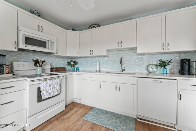 kitchen featuring light countertops, a sink, tasteful backsplash, light wood-style flooring, and white appliances