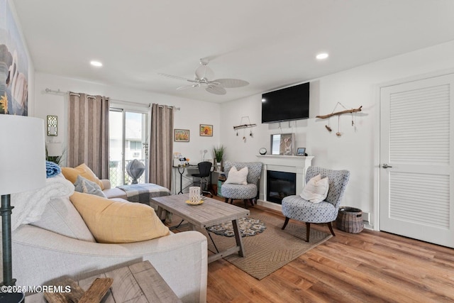 living area with a ceiling fan, recessed lighting, a glass covered fireplace, and wood finished floors