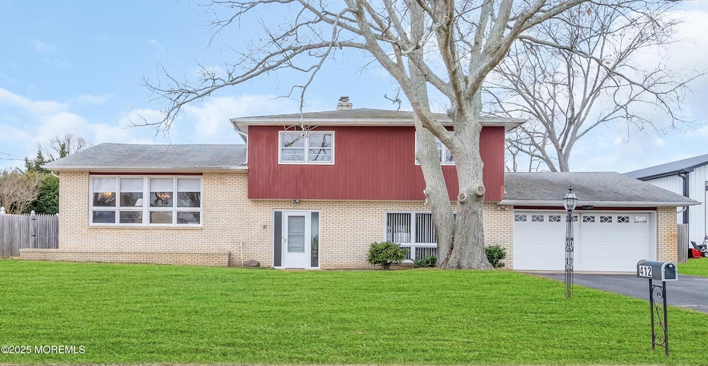 tri-level home with an attached garage, a front lawn, driveway, and a chimney
