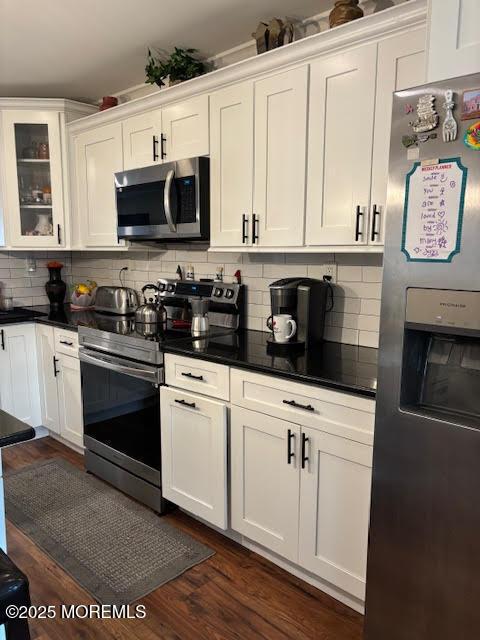 kitchen featuring glass insert cabinets, appliances with stainless steel finishes, white cabinets, dark countertops, and backsplash