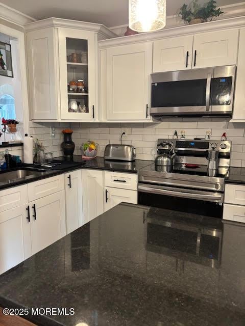 kitchen with appliances with stainless steel finishes, tasteful backsplash, white cabinets, and glass insert cabinets