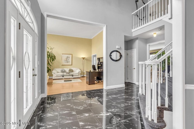 entryway with baseboards, marble finish floor, and a high ceiling
