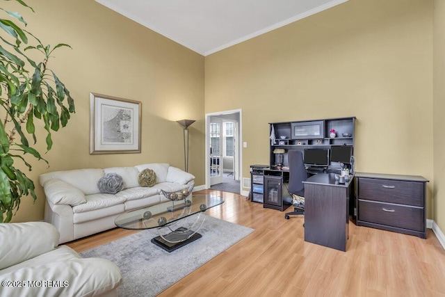 office space featuring light wood finished floors, a high ceiling, baseboards, and crown molding