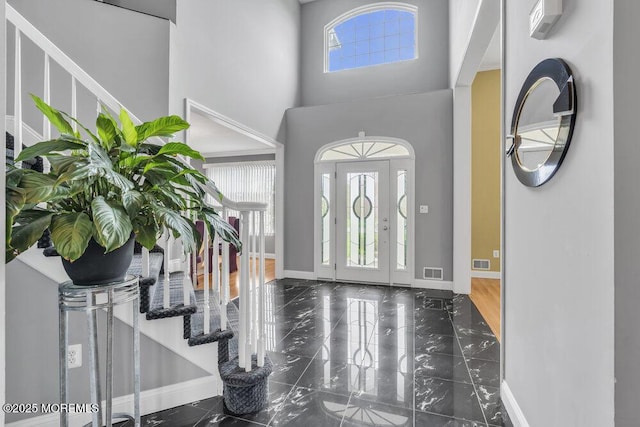foyer entrance featuring visible vents, baseboards, marble finish floor, and a high ceiling