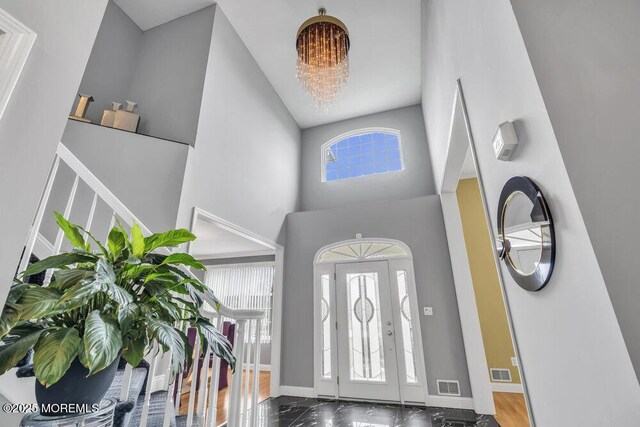 foyer entrance featuring baseboards, visible vents, and a towering ceiling
