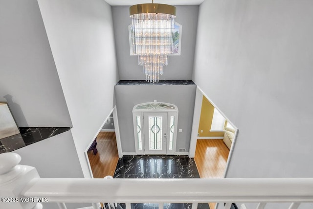 foyer entrance with a towering ceiling, a notable chandelier, baseboards, and wood finished floors