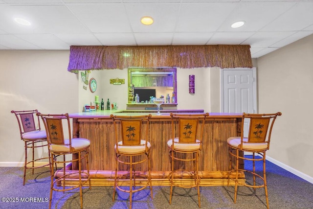 bar featuring a bar, carpet flooring, a drop ceiling, and baseboards
