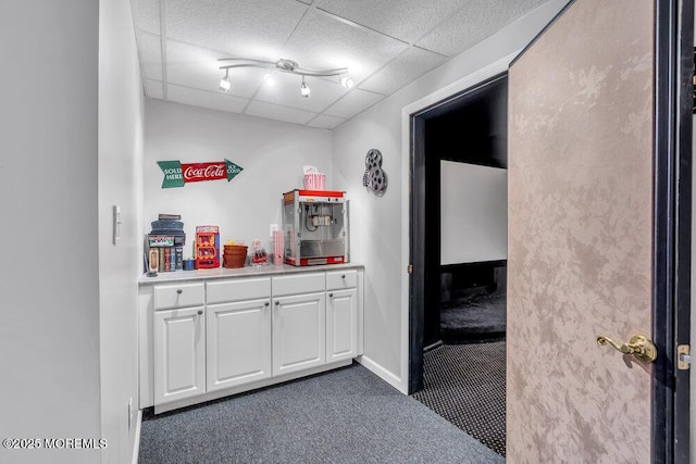 interior space with dark colored carpet, a drop ceiling, and baseboards