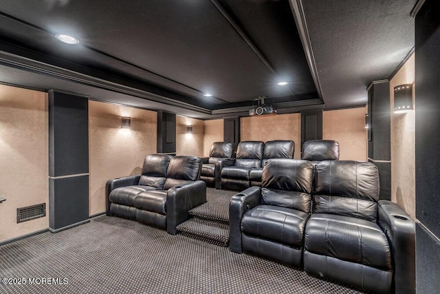 carpeted home theater room featuring a textured wall, visible vents, crown molding, and a raised ceiling