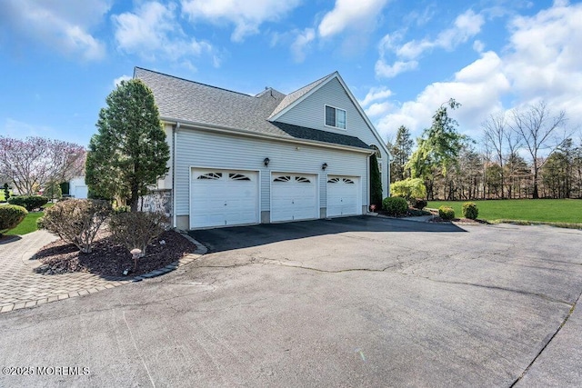 view of side of home with a garage, roof with shingles, driveway, and a lawn