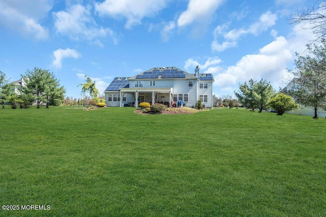 back of property featuring a yard and roof mounted solar panels