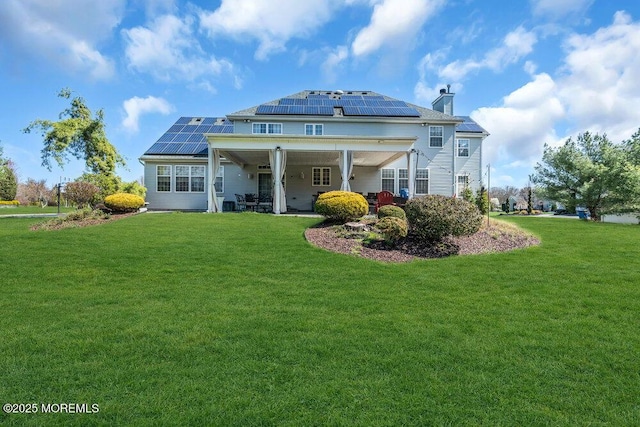back of property with a chimney, a lawn, and roof mounted solar panels