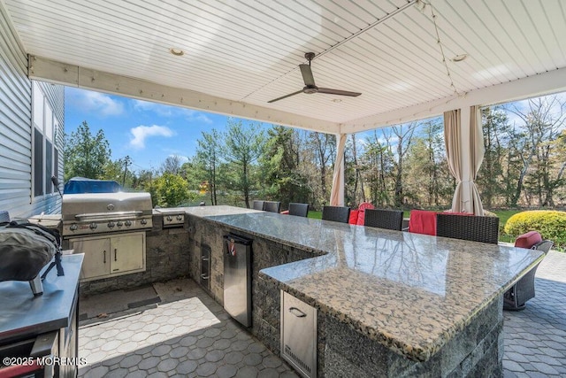 view of patio featuring a ceiling fan, outdoor wet bar, area for grilling, and an outdoor kitchen