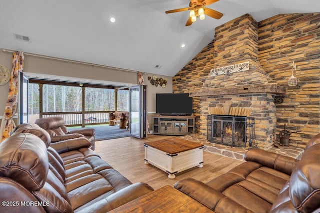living room with a large fireplace, light wood-style flooring, visible vents, ceiling fan, and high vaulted ceiling