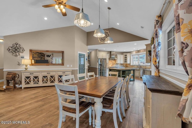 dining space featuring light wood-type flooring, high vaulted ceiling, ceiling fan, and visible vents